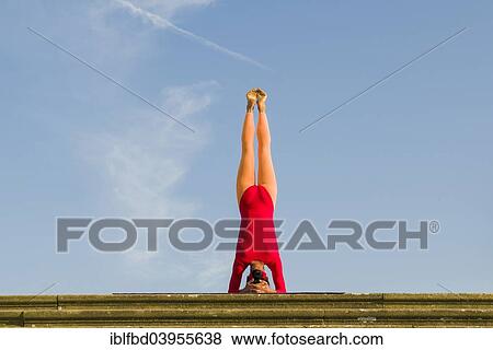 Stock Photo - "Young woman practising Hatha yoga, outdoors, showing the pose Sirshasana, Head stand". Fotosearch