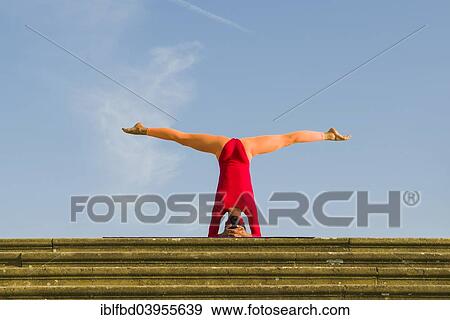 Stock Photo - "Young woman practising Hatha yoga, outdoors, showing the pose Sirshasana, Head stand". Fotosearch