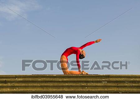 Stock Photo - "Young woman practising Hatha yoga, outdoors, showing the pose Ushtrasana, Camel pose". Fotosearch