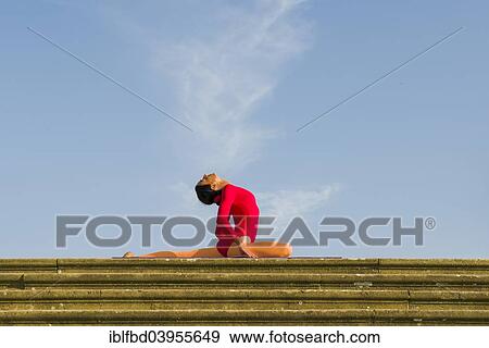 Stock Photo - "Young woman practising Hatha yoga, outdoors, showing the pose Kapotasana, Pigeon pose". Fotosearch