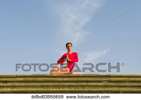Stock Photo - "Young woman practising Hatha yoga, outdoors, showing the pose Kapotasana, Pigeon pose". Fotosearch