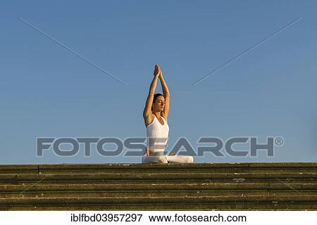 Stock Photo - "Young woman practising Hatha yoga, outdoors, showing the pose Padmasana, Lotus pose". Fotosearch