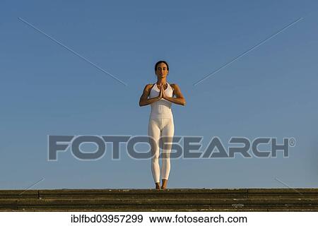 Stock Photo - "Young woman practising Hatha yoga, outdoors, showing the pose Tadasana, Pranamasana, Prayer pose". Fotosearch