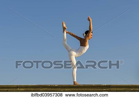 Stock Photo - "Young woman practising Hatha yoga, outdoors, showing the pose Saral natarajasana, Preparatory Lord Shiva's pose". Fotosearch