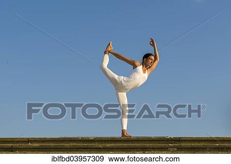 Stock Photo - "Young woman practising Hatha yoga, outdoors, showing the pose Saral natarajasana, Preparatory Lord Shiva's pose". Fotosearch