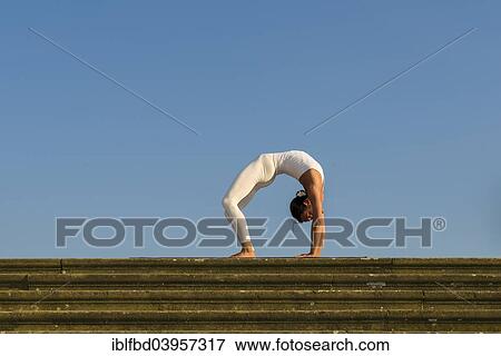 Stock Photo - "Young woman practising Hatha yoga, outdoors, showing the pose Chakrasana, Urdhva dhanurasana, Wheel pose". Fotosearch
