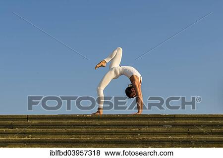 Stock Photo - "Young woman practising Hatha yoga, outdoors, showing the pose Chakrasana, Urdhva dhanurasana, Wheel pose". Fotosearch