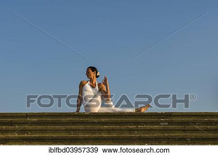 Stock Photo - "Young woman practising Hatha yoga, outdoors, showing the pose Ardha matsyendrasana, Half spinal twist". Fotosearch