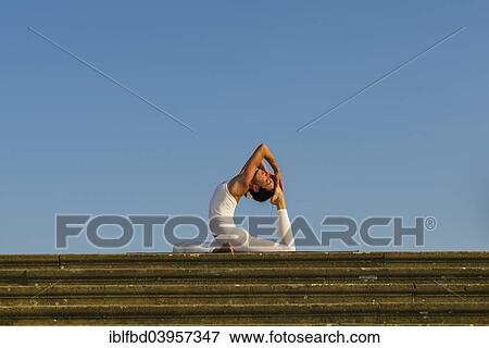 Stock Photo - "Young woman practising Hatha yoga, outdoors, showing the pose Kapotasana, Pigeon pose". Fotosearch