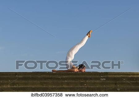 Stock Photo - "Young woman practising Hatha yoga, outdoors, showing the pose Shalabhasana, Locust". Fotosearch