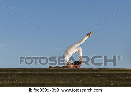 Stock Photo - "Young woman practising Hatha yoga, outdoors, showing the pose Shalabhasana, Locust". Fotosearch