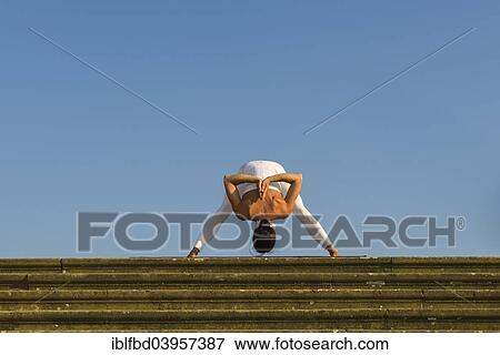 Stock Photo - "Young woman practising Hatha yoga, outdoors, showing the pose Prasarita padottanasana, Wide-legged forward bend". Fotosearch