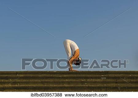 Stock Photo - "Young woman practising Hatha yoga, outdoors, showing the pose Pada hastasana or Uttanasana, Hand to foot pose, Intense foward-bending pose". Fotosearch