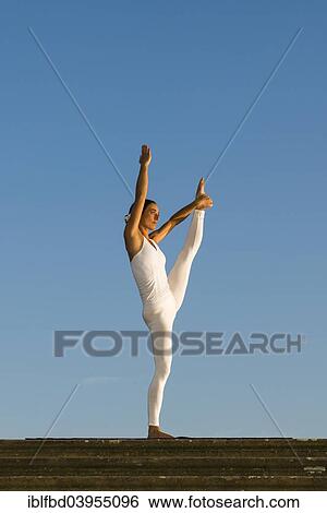 Stock Photograph - "Young woman practising Hatha yoga, outdoors, showing the pose Anjaneyasana, raised hand to foot pose". Fotosearch