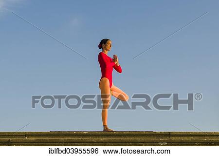Stock Photograph - "Young woman practising Hatha yoga, outdoors, showing the pose Vrikshasana, Tree". Fotosearch