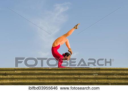 Stock Photograph - "Young woman practising Hatha yoga, outdoors, showing the pose Vrischikasana, Scorpion pose". Fotosearch