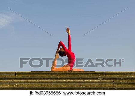 Stock Photograph - "Young woman practising Hatha yoga, outdoors, showing the pose Kapotasana, Pigeon pose". Fotosearch