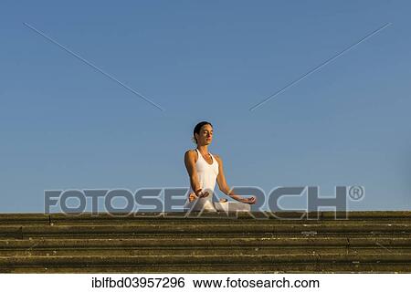 Stock Photograph - "Young woman practising Hatha yoga, outdoors, showing the pose Padmasana, Lotus pose". Fotosearch