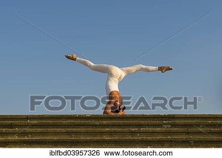 Stock Photograph - "Young woman practising Hatha yoga, outdoors, showing the pose Sirshasana, Head stand". Fotosearch