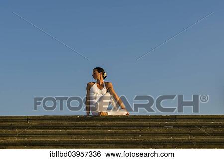 Stock Photograph - "Young woman practising Hatha yoga, outdoors, showing the pose Ardha matsyendrasana, Half spinal twist". Fotosearch