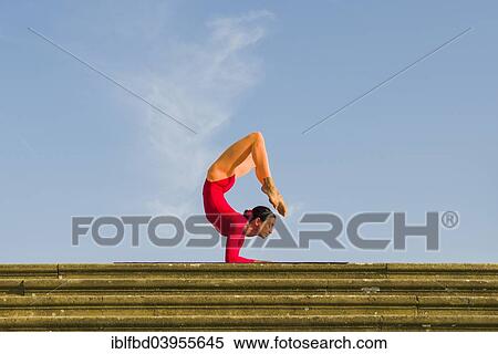 Stock Photography - "Young woman practising Hatha yoga, outdoors, showing the pose Vrischikasana, Scorpion pose". Fotosearch