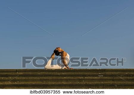 Stock Photography - "Young woman practising Hatha yoga, outdoors, showing the pose Bhujangasana, Cobra pose". Fotosearch