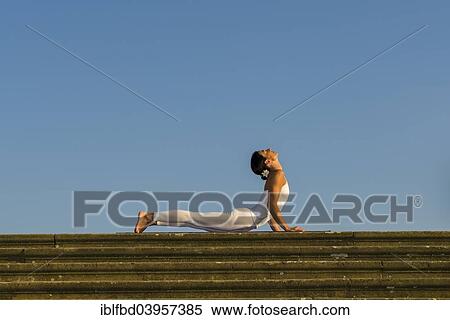 Stock Photography - "Young woman practising Hatha yoga, outdoors, showing the pose Bhujangasana, Cobra pose". Fotosearch