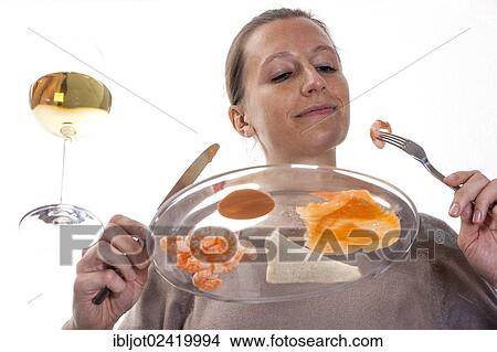 Young woman sitting at a glass table eating a cold fish dish, smoked salmon and shrimps with cocktail sauce View Large Photo Image Picture - Young woman sitting at a glass table eating a cold fish dish, smoked salmon and shrimps with cocktail sauce. Fotosearch