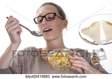 Stock Image - Young woman sitting at a glass table eating clear vegetable soup. Fotosearch