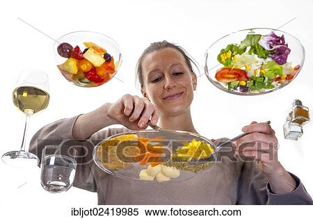 Stock Photography - Young woman sitting at a glass table eating steak with vegetables and potatoes, salad and fruit salad for dessert. Fotosearch