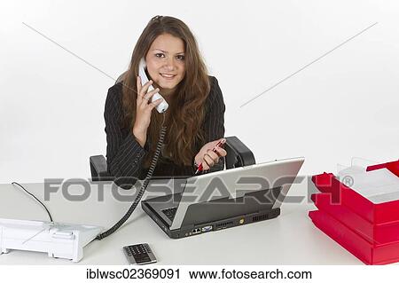 Young woman sitting at a laptop and holding a phone View Large Photo Image Stock Image - Young woman sitting at a laptop and holding a phone. Fotosearch