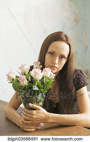 Stock Image - "Young woman sitting at a table with flowers in a vase, Germany, Europe". Fotosearch