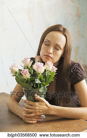 Stock Image - "Young woman sitting at a table with flowers in a vase, Germany, Europe". Fotosearch