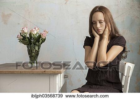 Stock Photo - "Young woman sitting at a table with flowers in a vase, Germany, Europe". Fotosearch