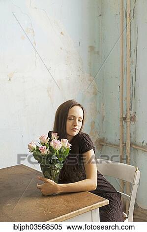 Stock Photography - "Young woman sitting at a table with flowers in a vase, Germany, Europe". Fotosearch