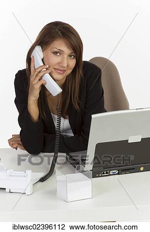 "Young woman sitting at desk with laptop, on the phone" View Large Photo Image Stock Image - "Young woman sitting at desk with laptop, on the phone". Fotosearch