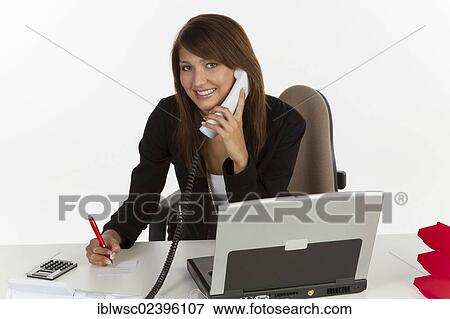 "Young woman sitting at desk with laptop, on the phone" View Large Photo Image Stock Photo - "Young woman sitting at desk with laptop, on the phone". Fotosearch