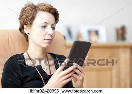 Young woman sitting in an armchair and reading an e-book, Grevenbroich, North Rhine-Westphalia, Grevenbroich, Germany, Europe View Large Photo Image Stock Photograph - Young woman sitting in an armchair and reading an e-book, Grevenbroich, North Rhine-Westphalia, Grevenbroich, Germany, Europe. Fotosearch