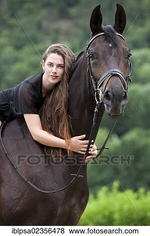 Stock Photo - "Young woman sitting on a horse and cuddling its neck, Hanoverian horse, bay, North Tyrol, Austria, Europe". Fotosearch