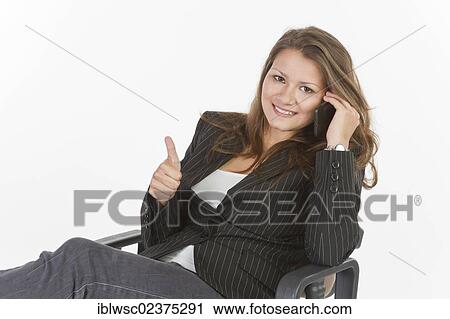Stock Image - "Young woman sitting on an office chair, making thumbs up gesture". Fotosearch