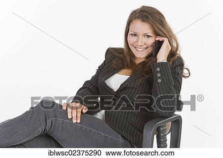 Stock Image - Young woman sitting on office chair making a phone call. Fotosearch