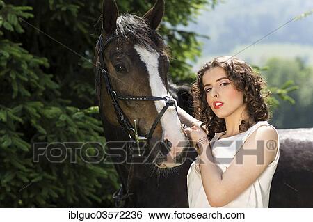 Young woman standing beside a horse View Large Photo Image Stock Photograph - Young woman standing beside a horse. Fotosearch