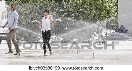 Stock Photo - "Young woman standing in the park, water from a sprinkler system splashing her body, Innsbruck, Tyrol, Austria, Europe". Fotosearch