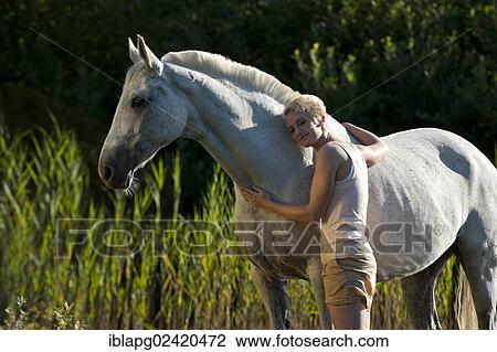 Stock Image - Young woman standing with a Hanoverian horse. Fotosearch