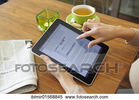 Stock Photography - Young woman using an iPad tablet computer at a cafe table. Fotosearch