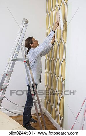 Stock Photo - Young woman wallpapering a wall. Fotosearch