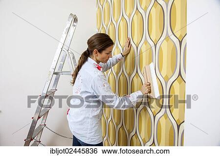 Young woman wallpapering a wall View Large Photo Image Stock Photograph - Young woman wallpapering a wall. Fotosearch