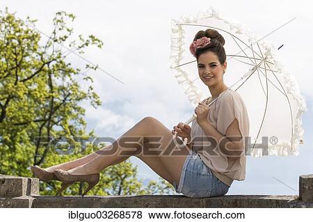 Stock Photo - "Young woman wearing a beige top and jeans hot pants, holding a parasol". Fotosearch