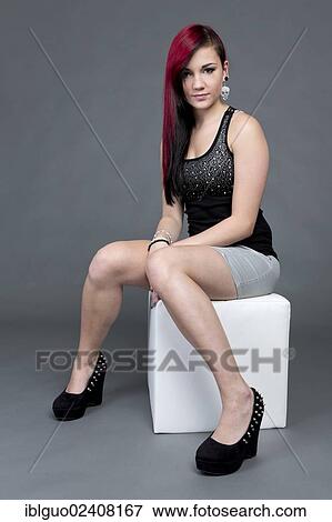 "Young woman wearing a black top, a short gray skirt and high heels posing on a cube seat" View Large Photo Image Stock Photo - "Young woman wearing a black top, a short gray skirt and high heels posing on a cube seat". Fotosearch