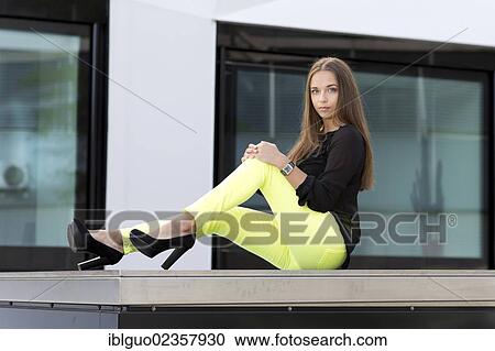 Stock Image - "Young woman wearing a black top, bright yellow trousers and high black shoes". Fotosearch